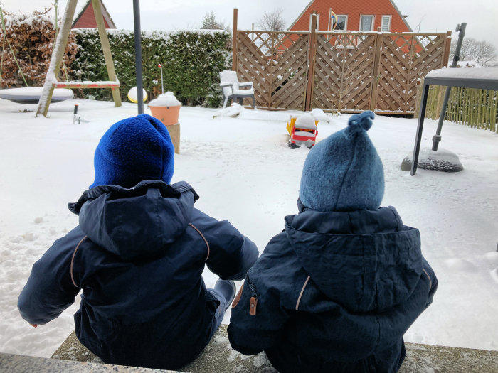2 Kinder schauen in den schneebedeckten Garten
